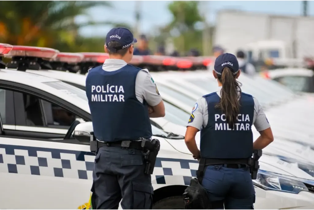 Dois policiais da Policia Militar do Distrito Federal (PM DF) parados de costas em frente a viatura